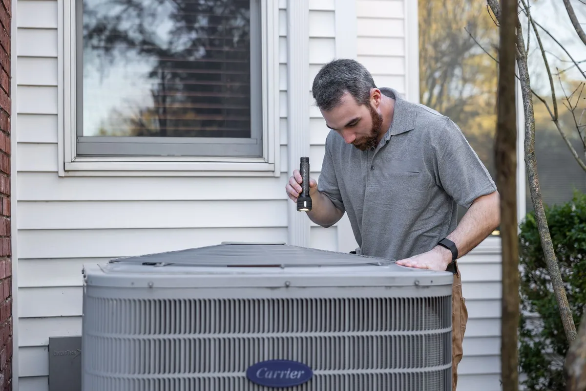A home-services technician inspecting an outdoor HVAC unit on a service call