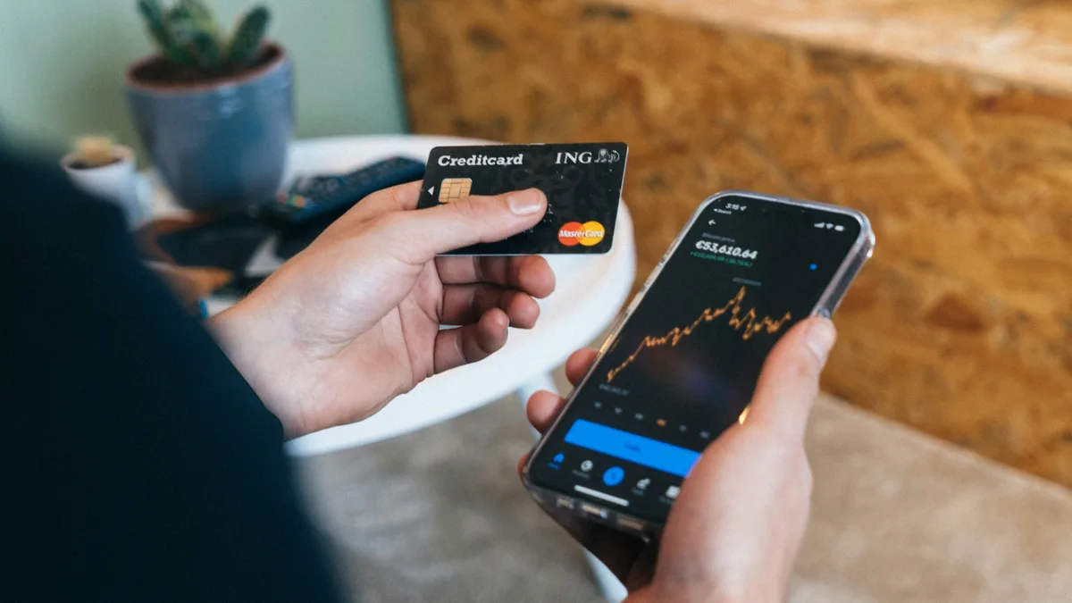 A person holding a smartphone showing a chart in one hand and a credit card in the other