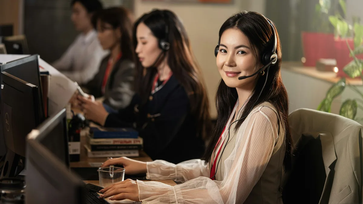 A smiling customer service agent wearing a headset at a computer in a call center