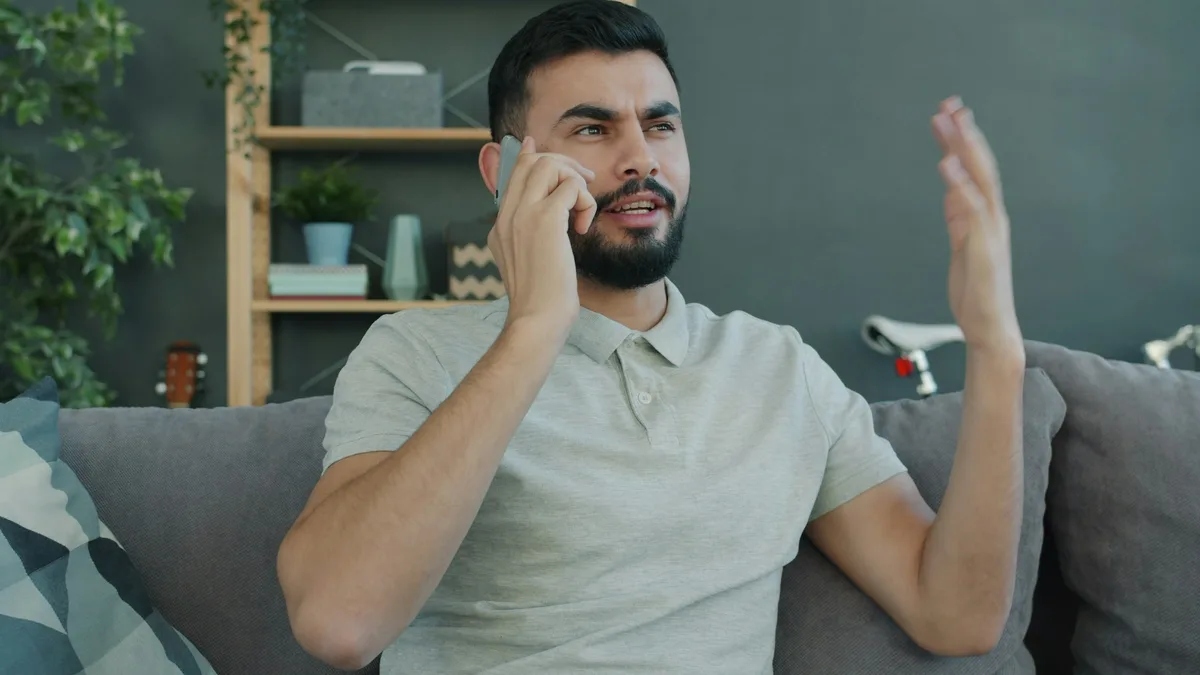 A man sitting on a couch talking animatedly on the phone