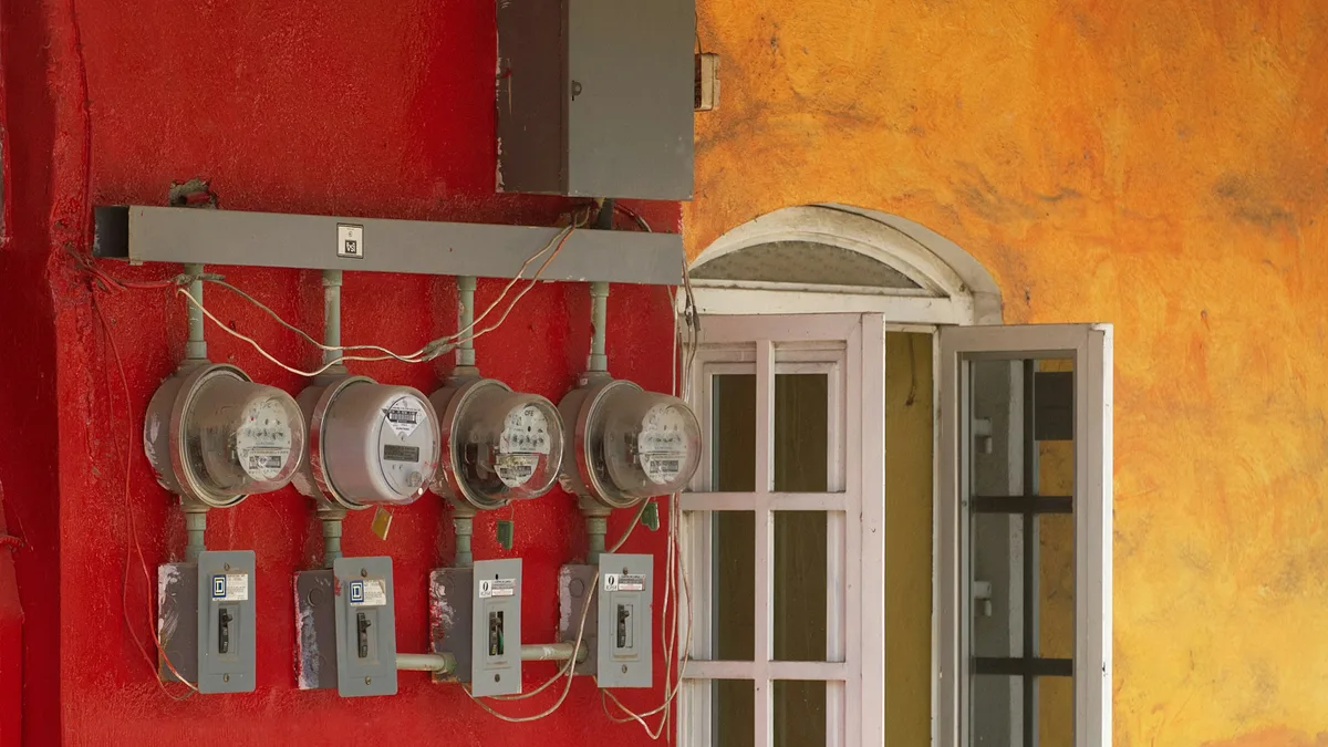 Four electric meters mounted in a row on a red wall beside a window